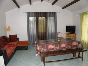 A room with a sofa, a table with a floral tablecloth, a television on a cabinet, and curtains on the windows. - Villas with private pools in the Cévennes near Ardèche   (SAINT BRES)