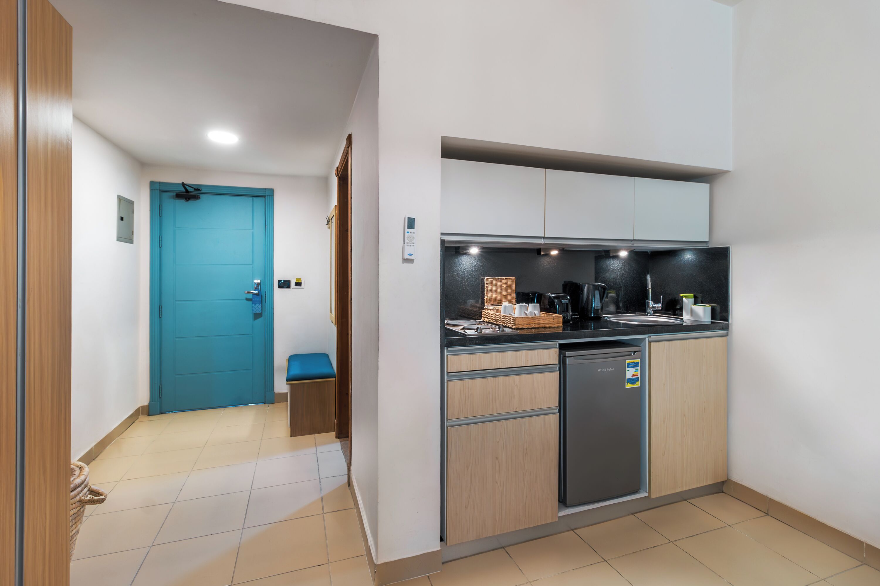A compact kitchen with a blue door, a small seating area, and a refrigerator.