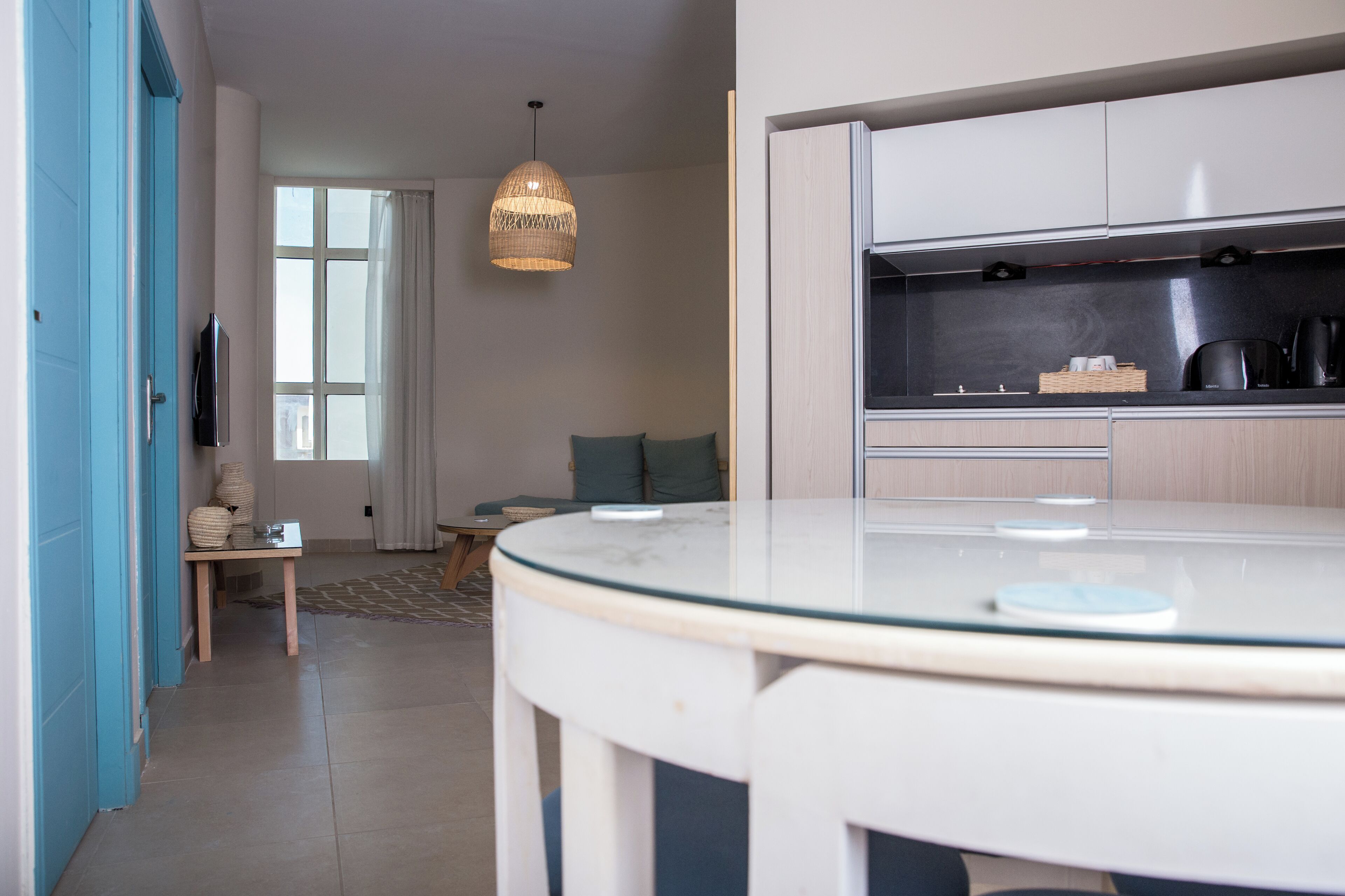Een moderne keuken met een ronde glazen tafel, een hanglamp en uitzicht op de woonkamer.