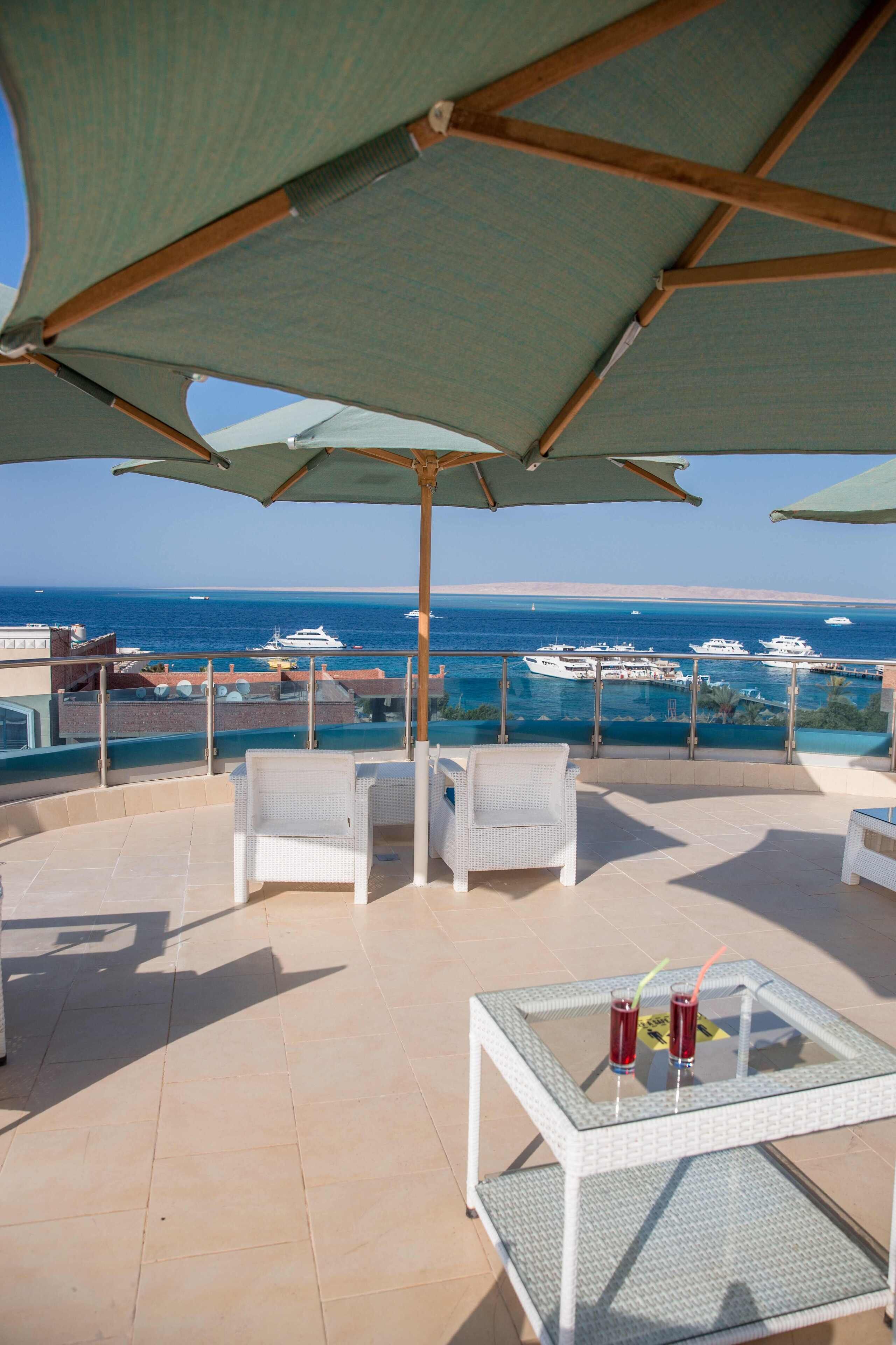 Une terrasse dotée de meubles en osier blanc, une table en verre avec des boissons, et une vue sur la mer et les yachts.