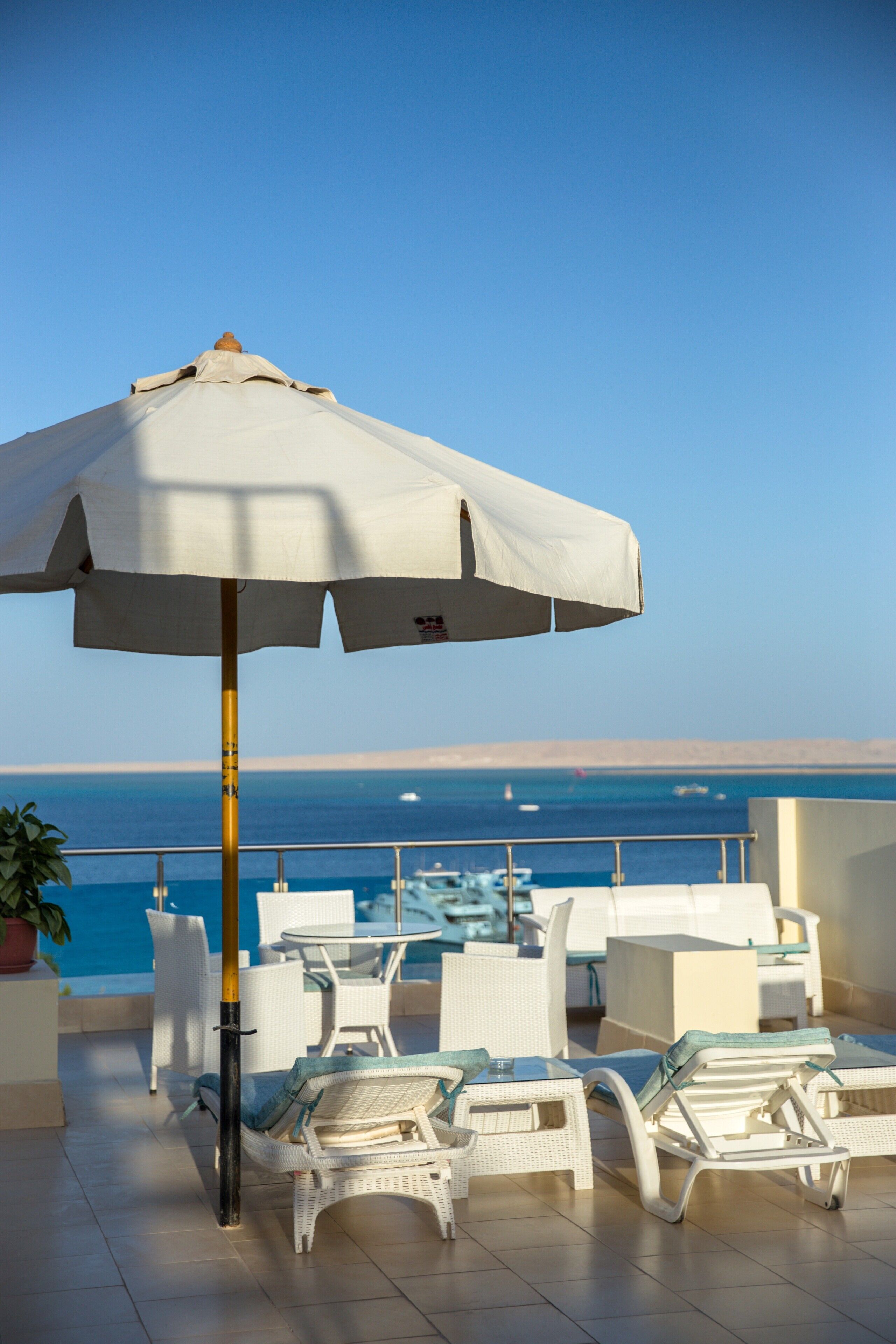 A terrace with white lounge chairs, a table, and an umbrella.