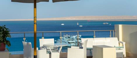 A terrace with white lounge chairs, a table, and an umbrella.