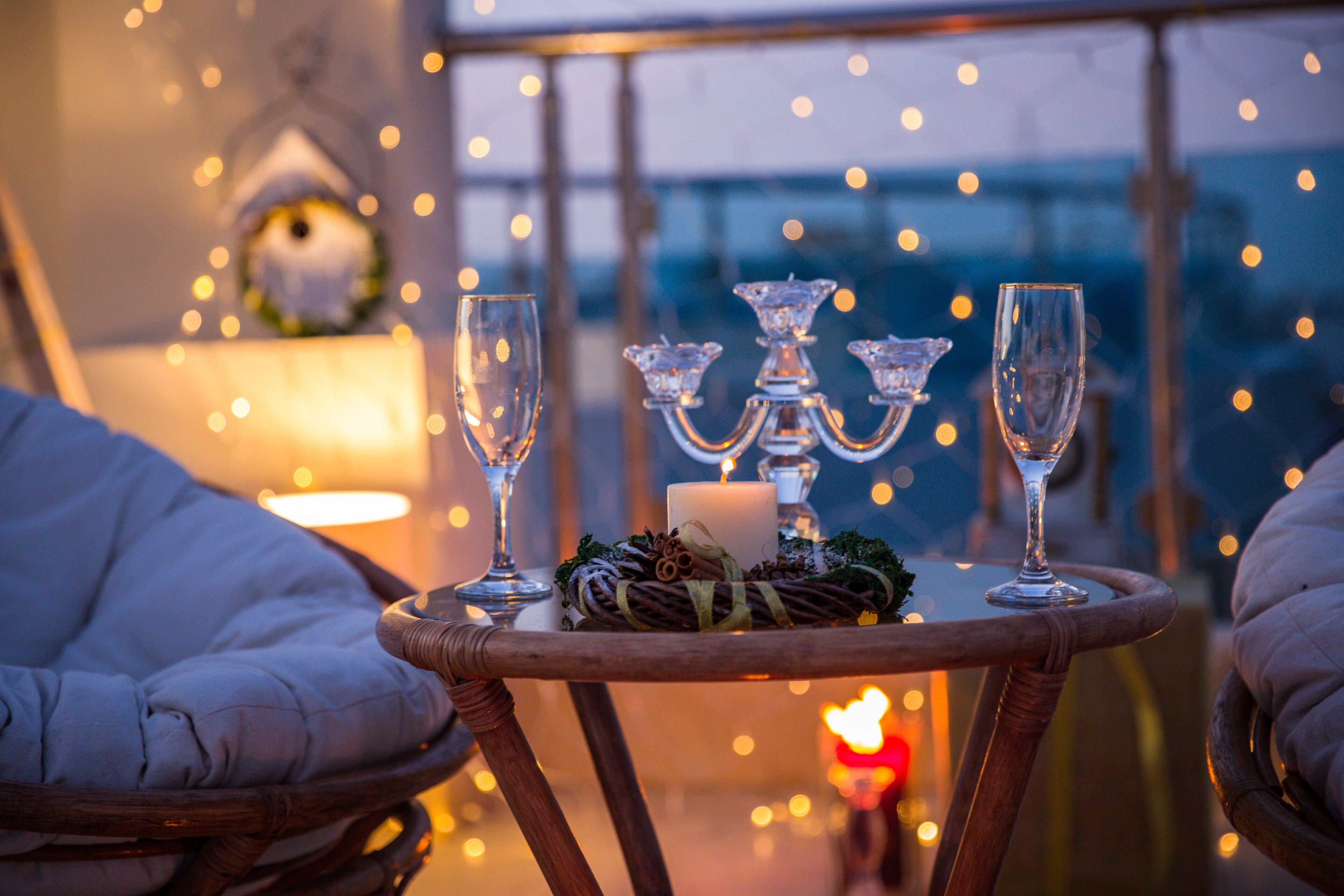 A cozy outdoor seating area with wicker chairs, a small round table with candles and glasses, and a view of the cityscape at dusk.