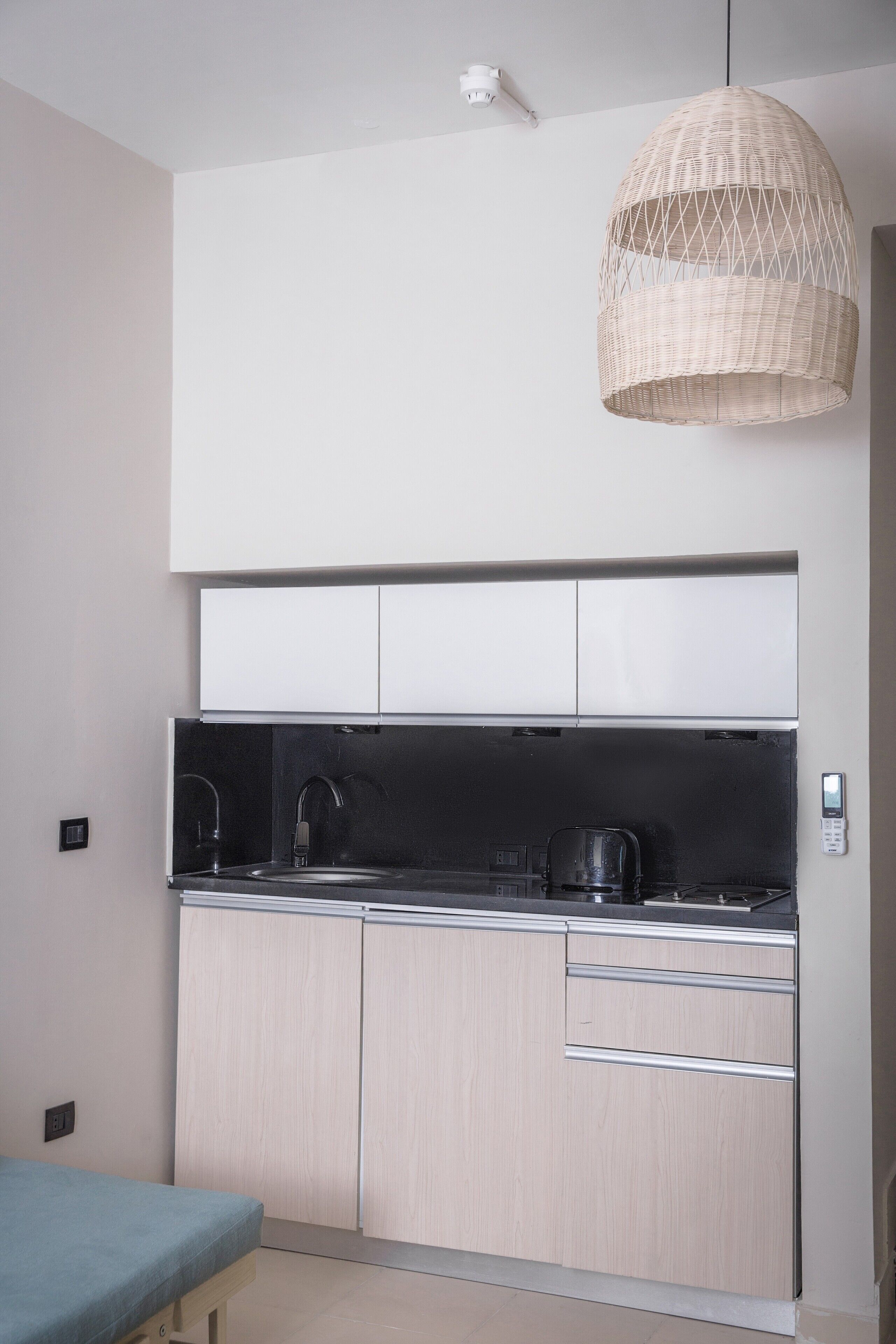 A compact kitchen with a hanging light fixture, a sink, and cabinets.