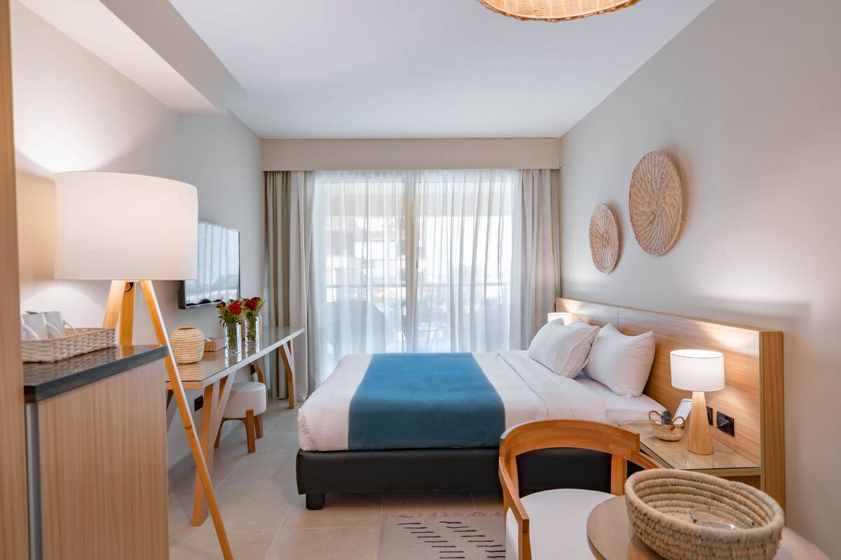 A hotel room with a bed, bedside table, lamp, and a desk with a chair.