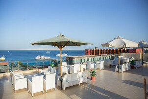 Una terraza en la azotea con muebles de mimbre blanco, un paraguas verde y vistas al mar y a los barcos.