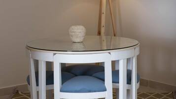A round glass table with white legs and blue cushioned chairs, a white lamp with a wooden stand, and a patterned floor.