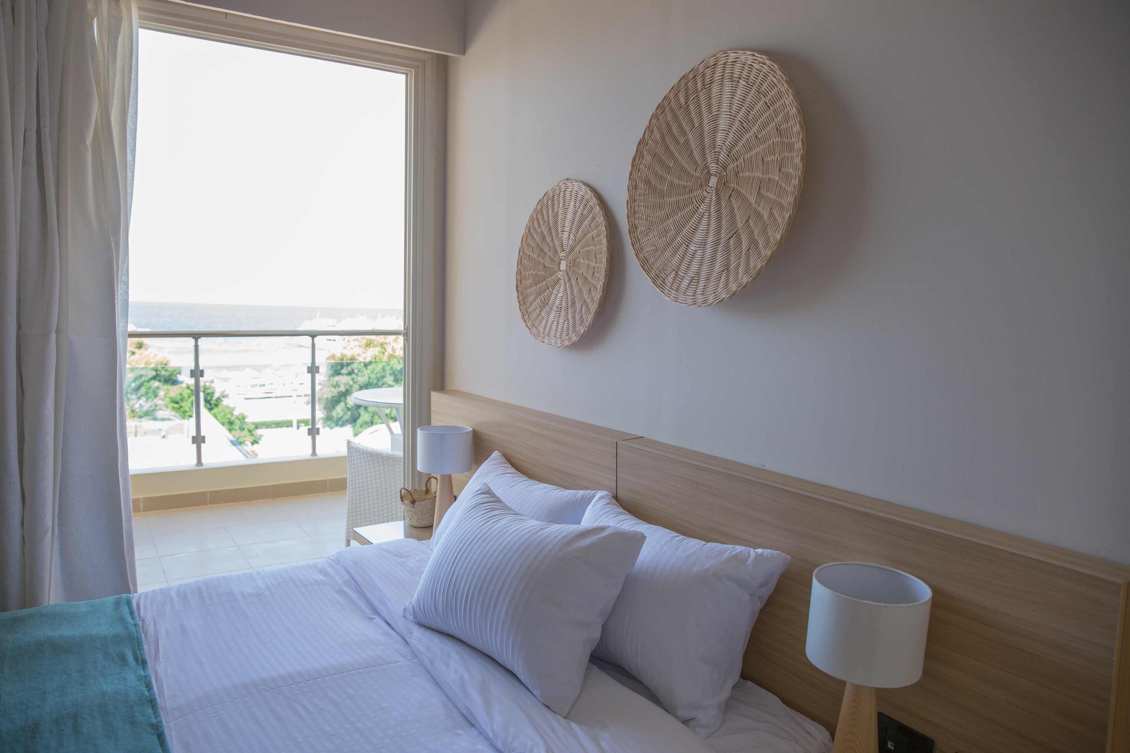Habitación de hotel con una cama grande, dos cestas tejidas en la pared, vista al mar y un balcón con barandilla.