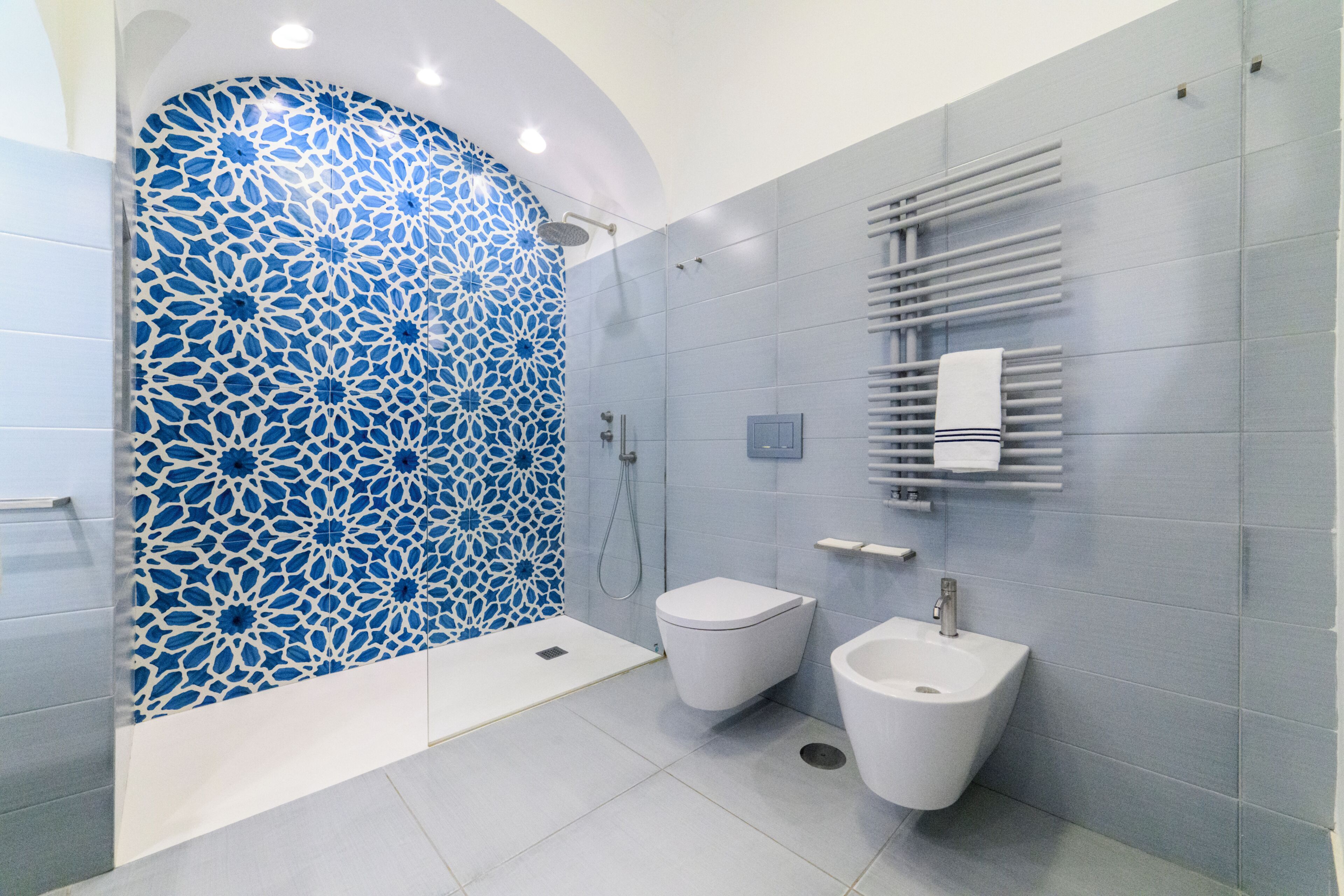 A modern bathroom with a patterned wall, a shower, a bidet, and a sink.