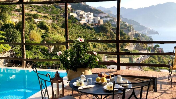 A terrace with a pool, dining table, and chairs, overlooking a hillside town and the sea. - Villa Alba d' Oro - Historic Luxury Villa  (Amalfi)
