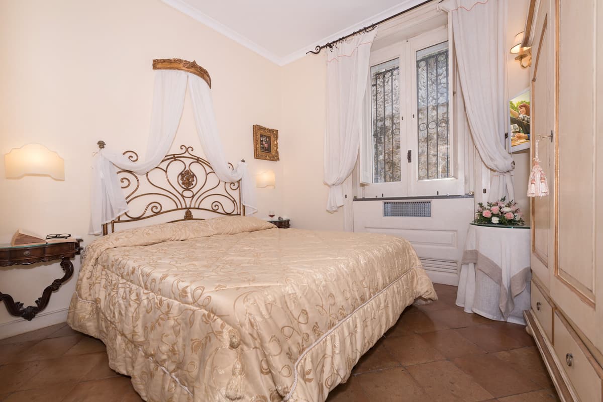Une chambre avec un grand lit, une table de chevet, une fenêtre avec des rideaux et une lampe fixée au mur.