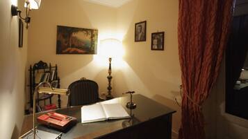 Una habitación con escritorio, silla, lámpara y ventana con cortinas.