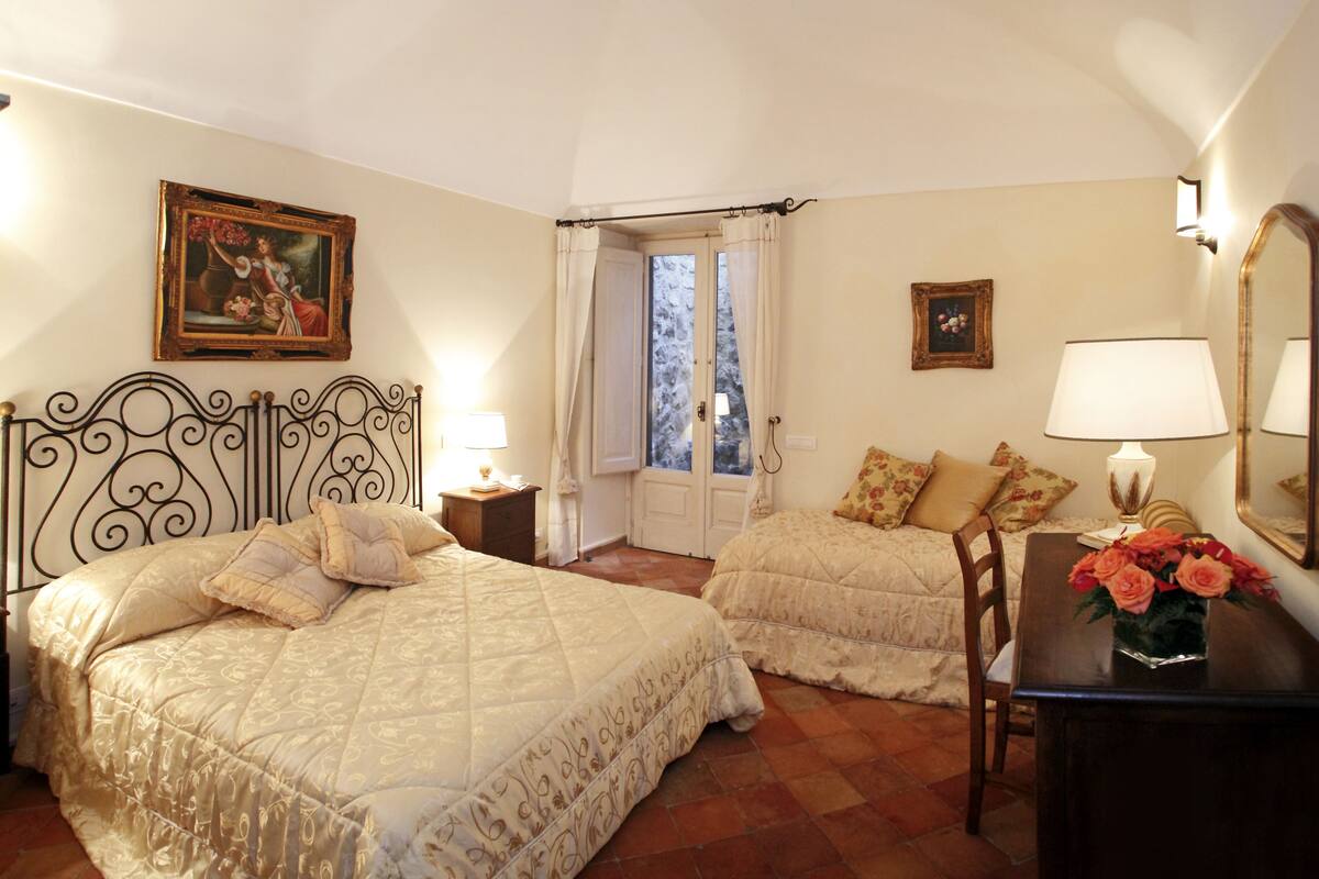 Une chambre avec deux lits, un bureau avec une lampe, une chaise et une fenêtre avec des rideaux.