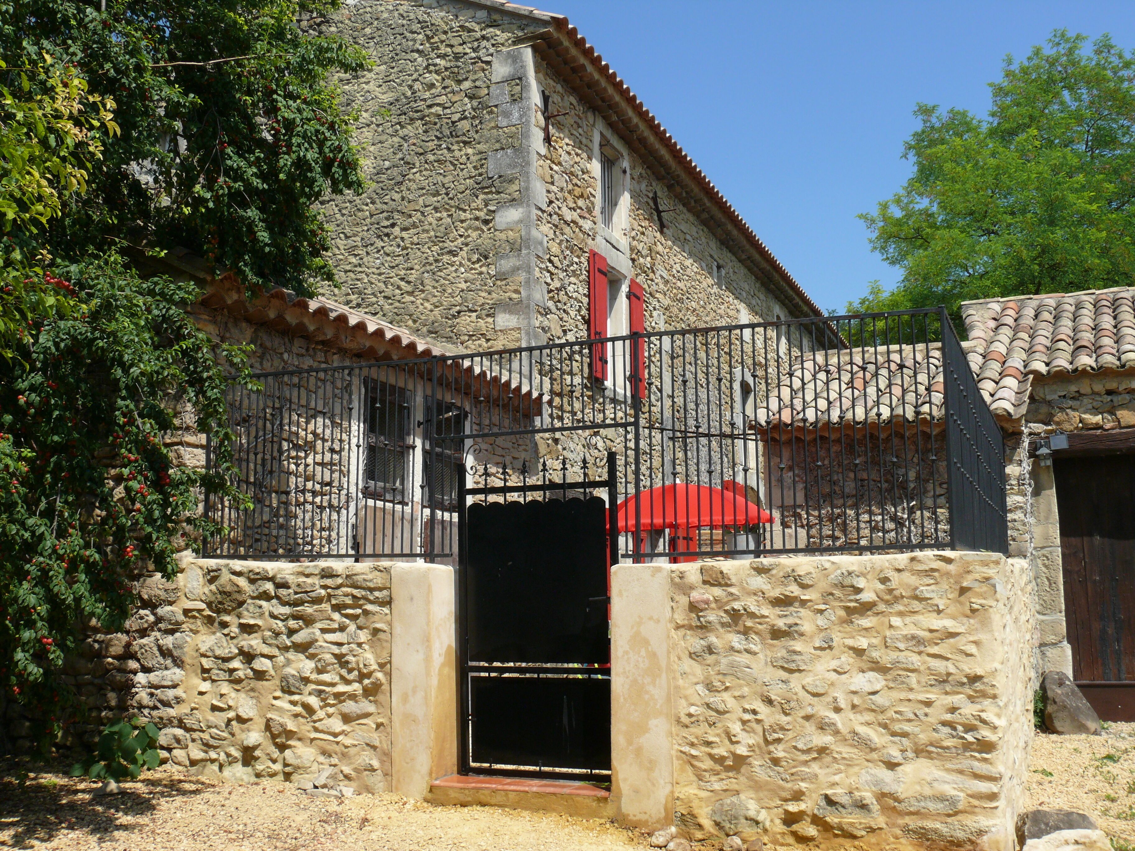 Un bâtiment en pierre avec un portail en métal, un parapluie rouge et un escalier menant à une porte.