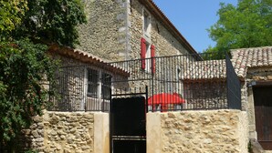 A stone building with a metal gate, a red umbrella, and a staircase leading to a door. - Superb Gîte in Mas (Bollène)