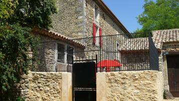 Un bâtiment en pierre avec un portail en métal, un parapluie rouge et un escalier menant à une porte.