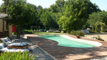 Une piscine dotée d’une terrasse en bois, entourée de gravier, d’arbres et de mobilier d’extérieur.