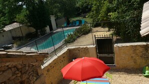 A pool area with a stone wall, a red umbrella, and a striped table. - Superb Gîte in Mas (Bollène)