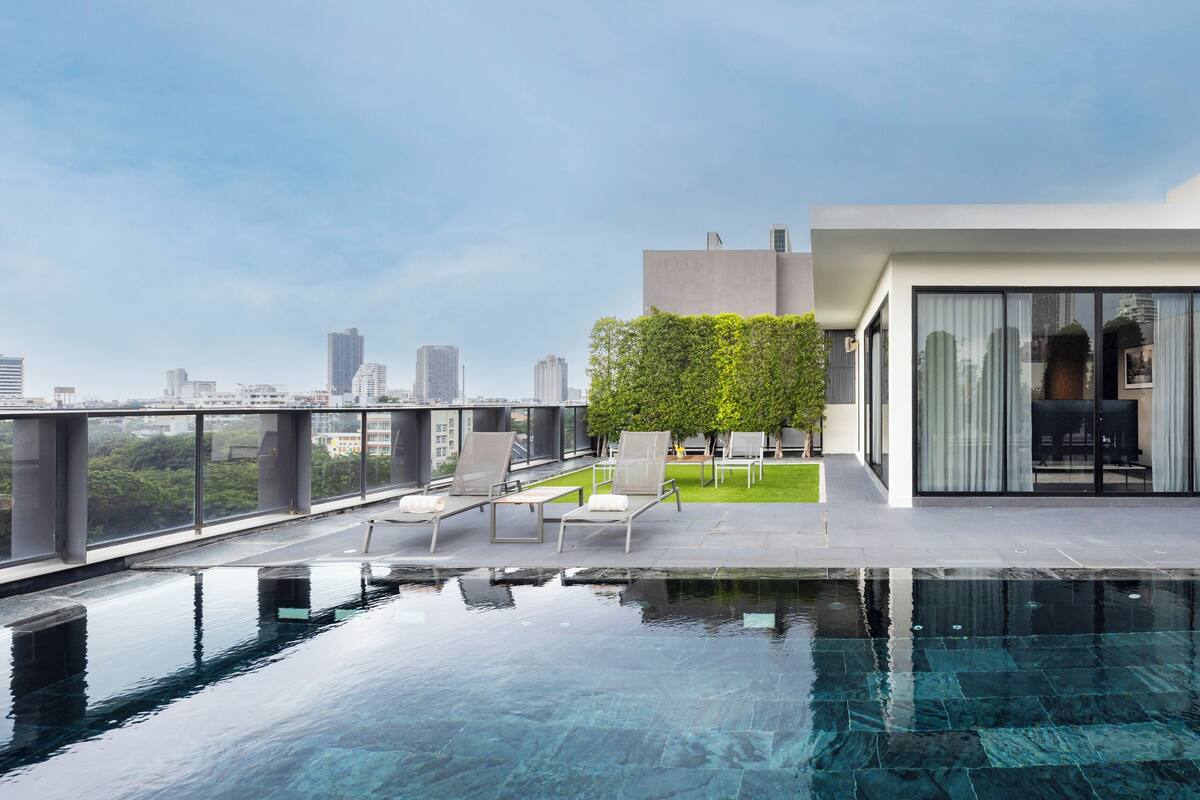 Une piscine moderne située sur un toit, avec une eau d’un bleu cristallin, entourée de chaises longues et offrant une vue sur le paysage urbain.