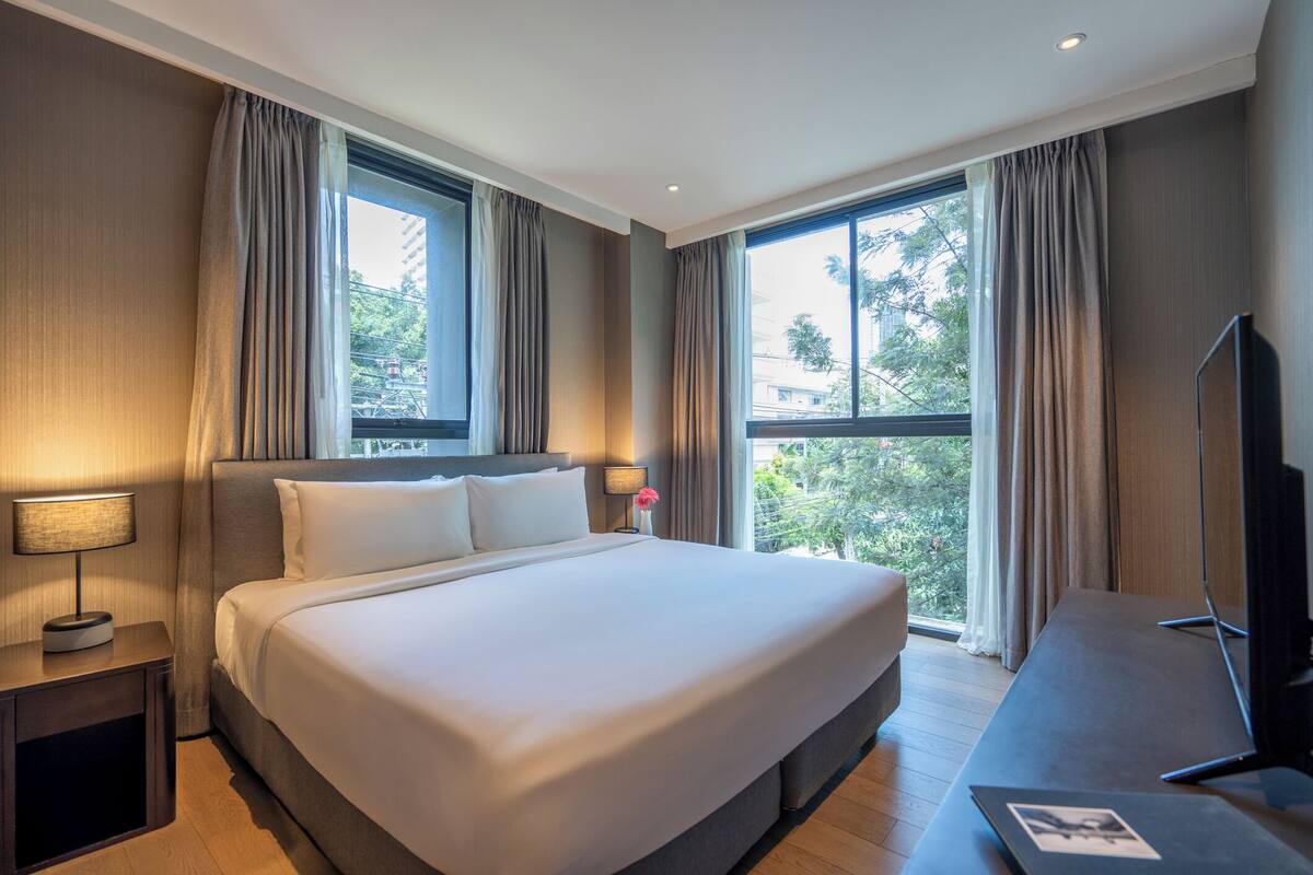 Une chambre d’hôtel avec un grand lit, un bureau, une télévision et une fenêtre avec des rideaux.