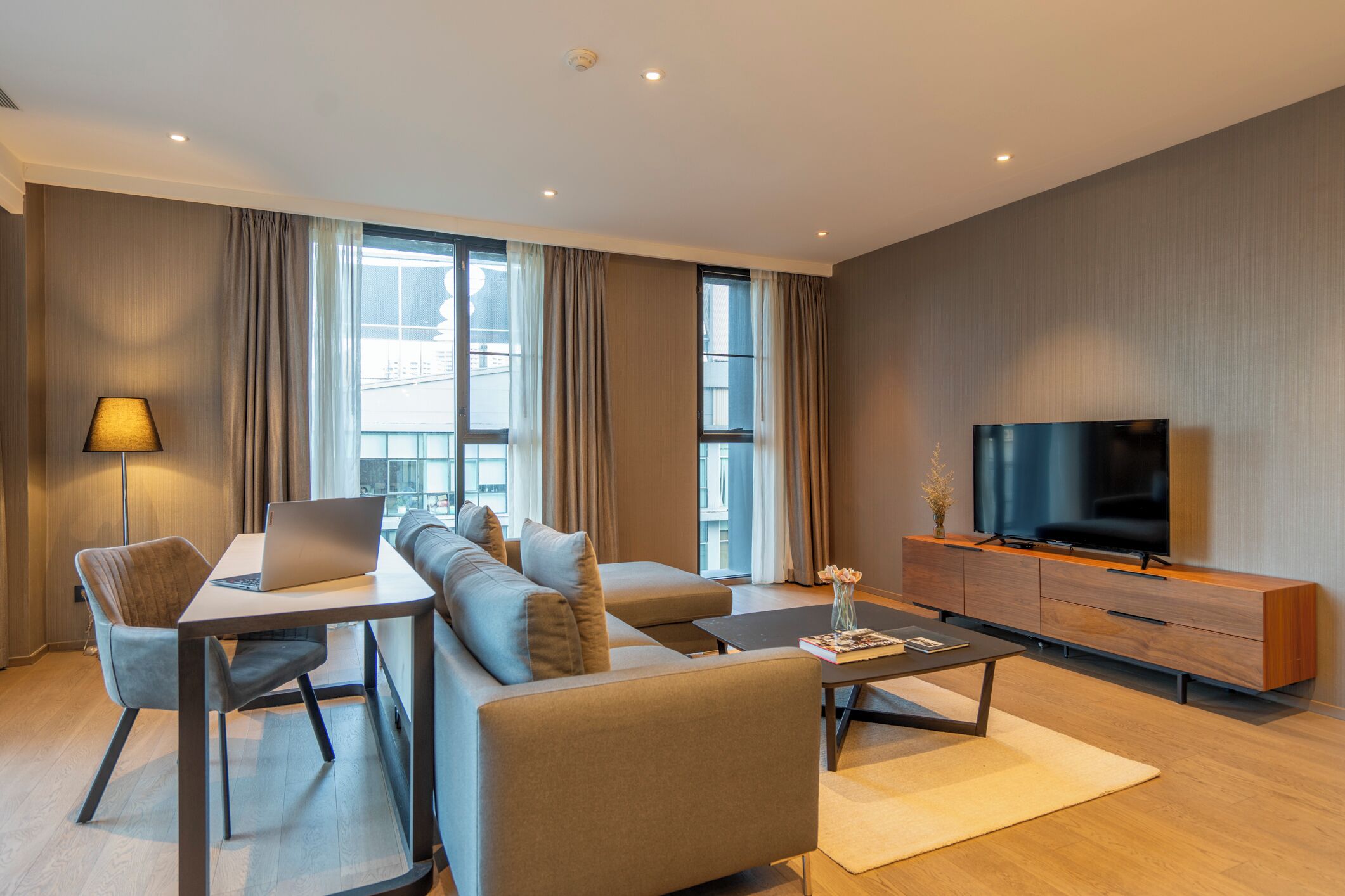 A modern living room with a sofa set, a coffee table, a TV, and a laptop on a desk.