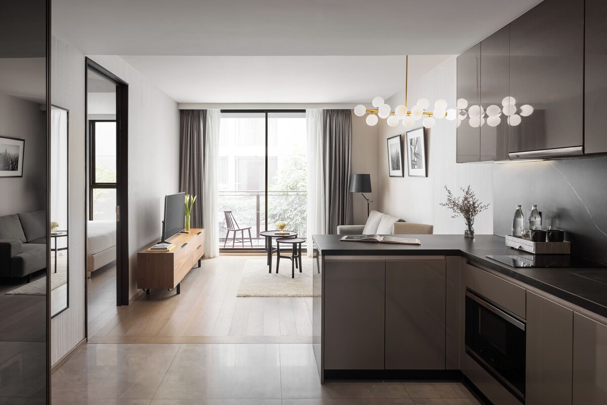 Une cuisine moderne dotée d’un îlot central, un coin repas avec une table et des chaises, et un espace de vie avec un canapé et un téléviseur.