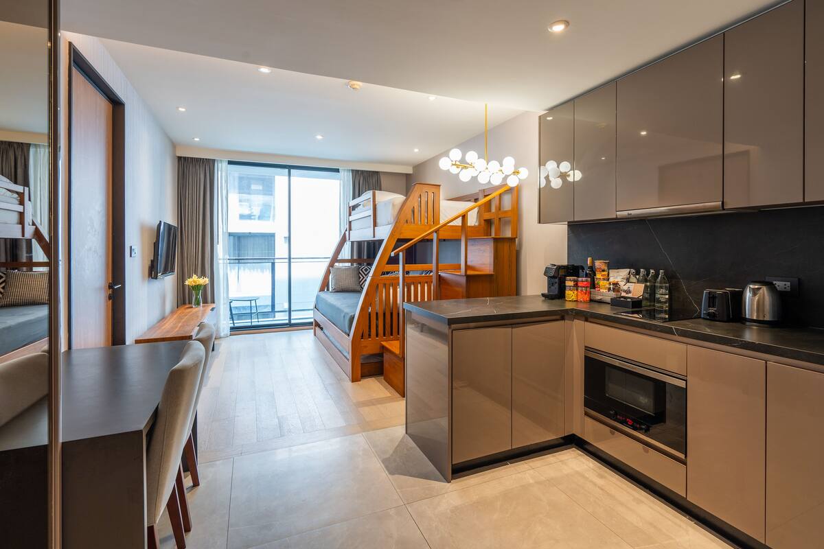 Une cuisine moderne dotée d’un four encastré, un coin repas avec un banc et un escalier menant à un balcon.