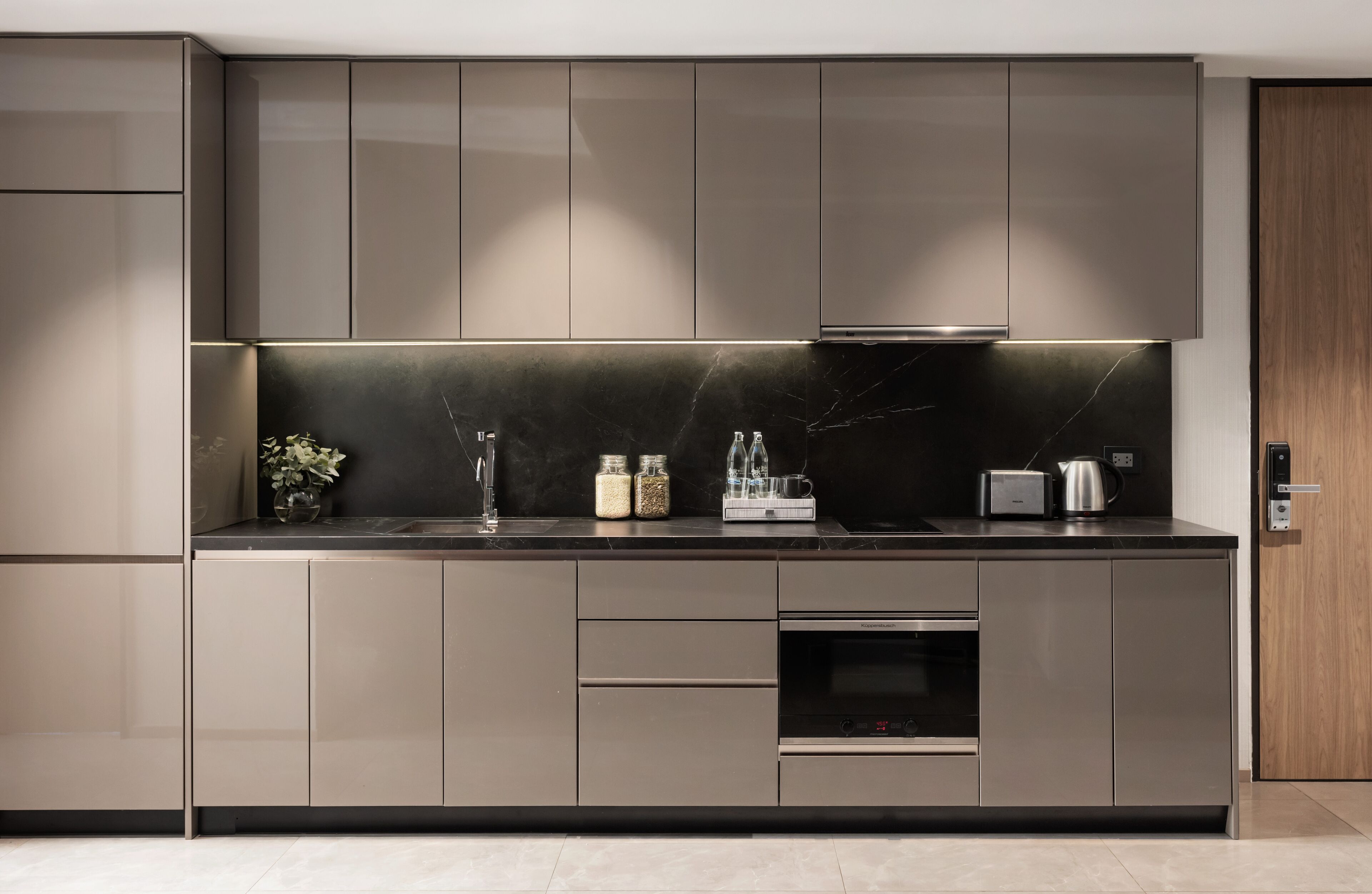 A modern kitchen with sleek cabinetry, a black marble backsplash, and stainless steel appliances.