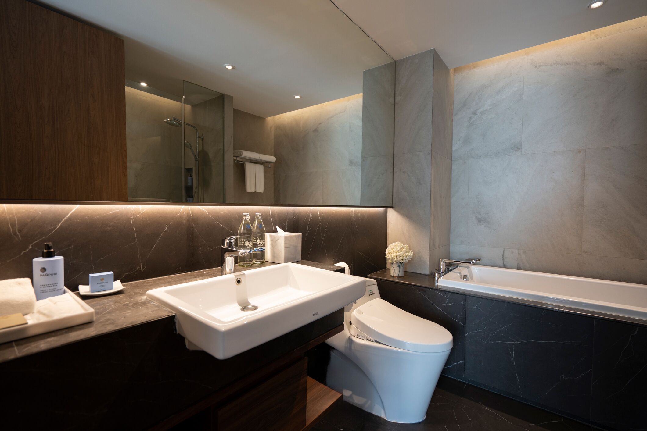 A modern bathroom with a large mirror, a white sink, a bathtub, and a toilet.