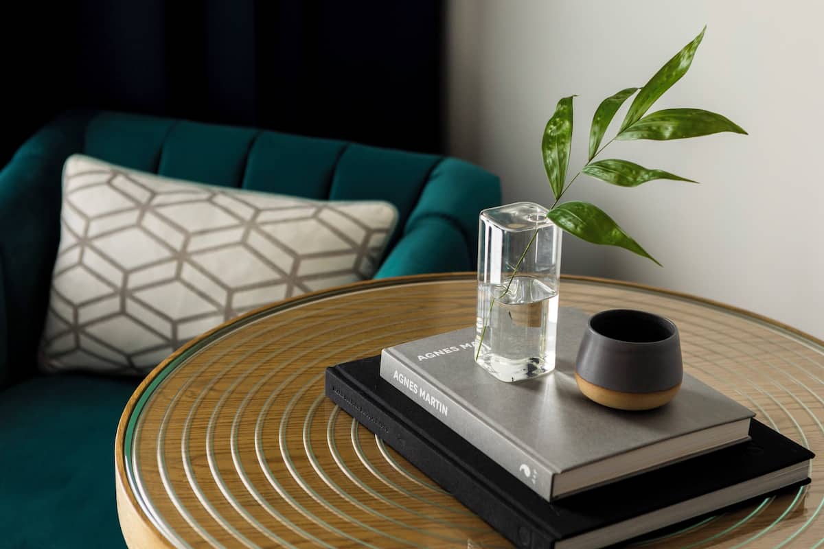 A round glass table with a book, a glass vase with a plant, and a mug.
