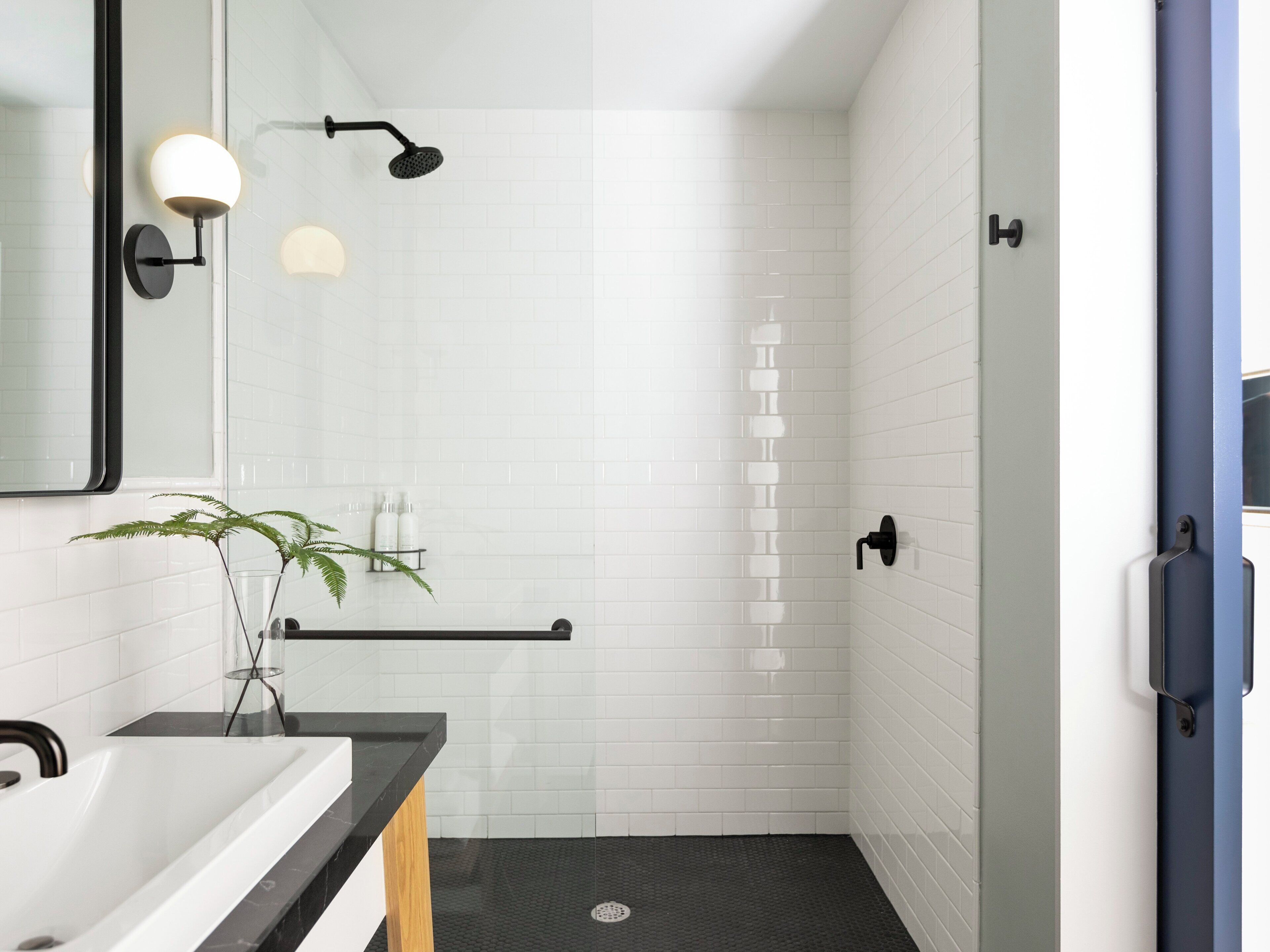 A modern bathroom with a white tiled shower, a black bathtub, and a mirror with a black frame.