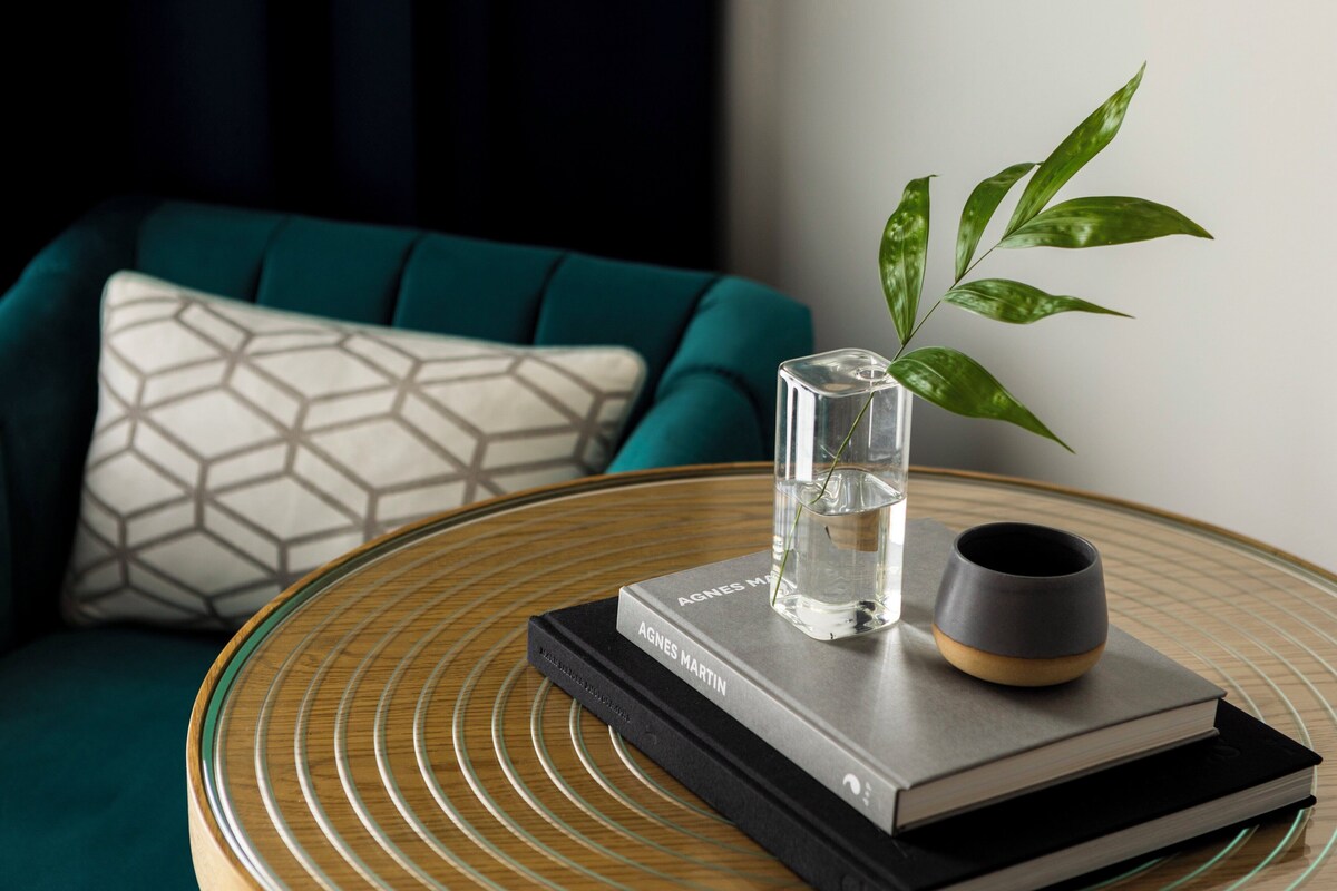 A round glass table with a book, a glass vase with a plant, and a cup.
