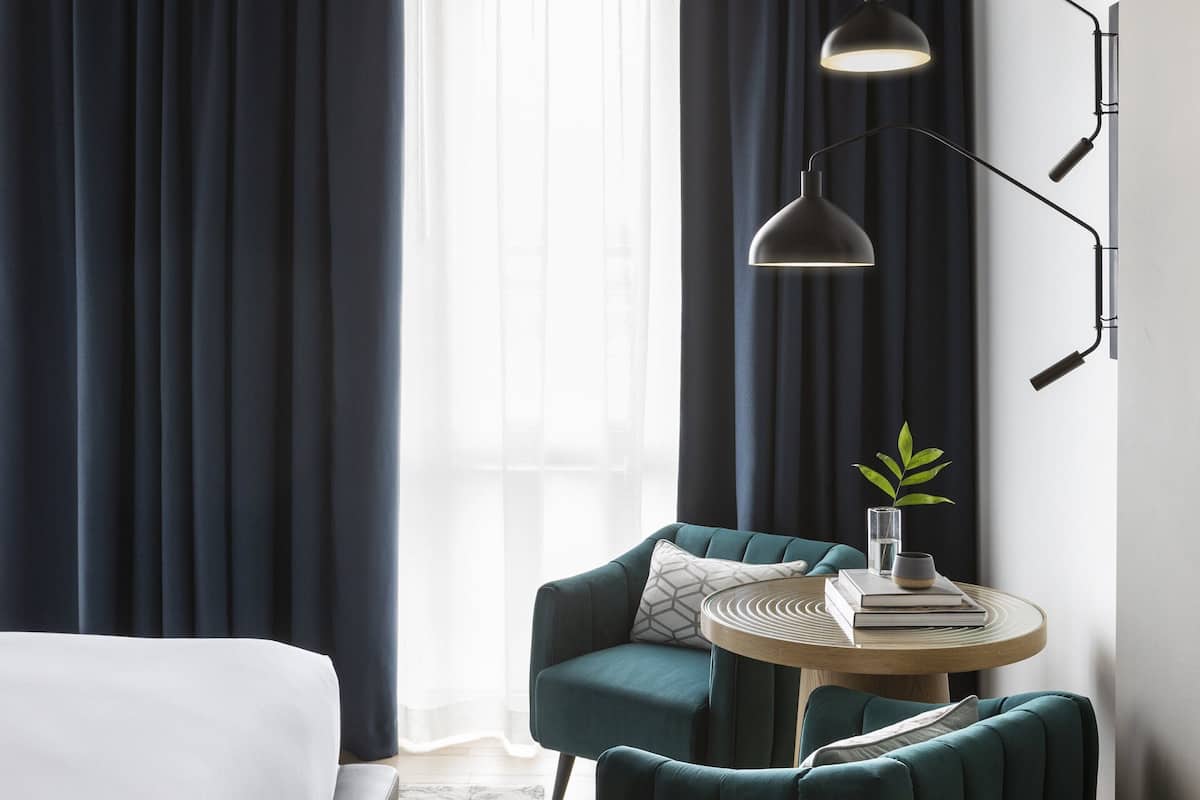 A modern hotel room with a bed, a sofa, a round table with a plant, and a floor lamp.