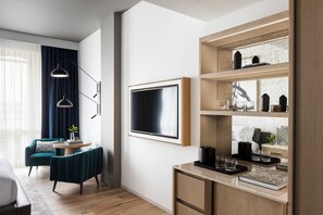 A modern living room with a sofa, a coffee table, and a TV. There is a bookshelf with decorative items and a window with curtains.