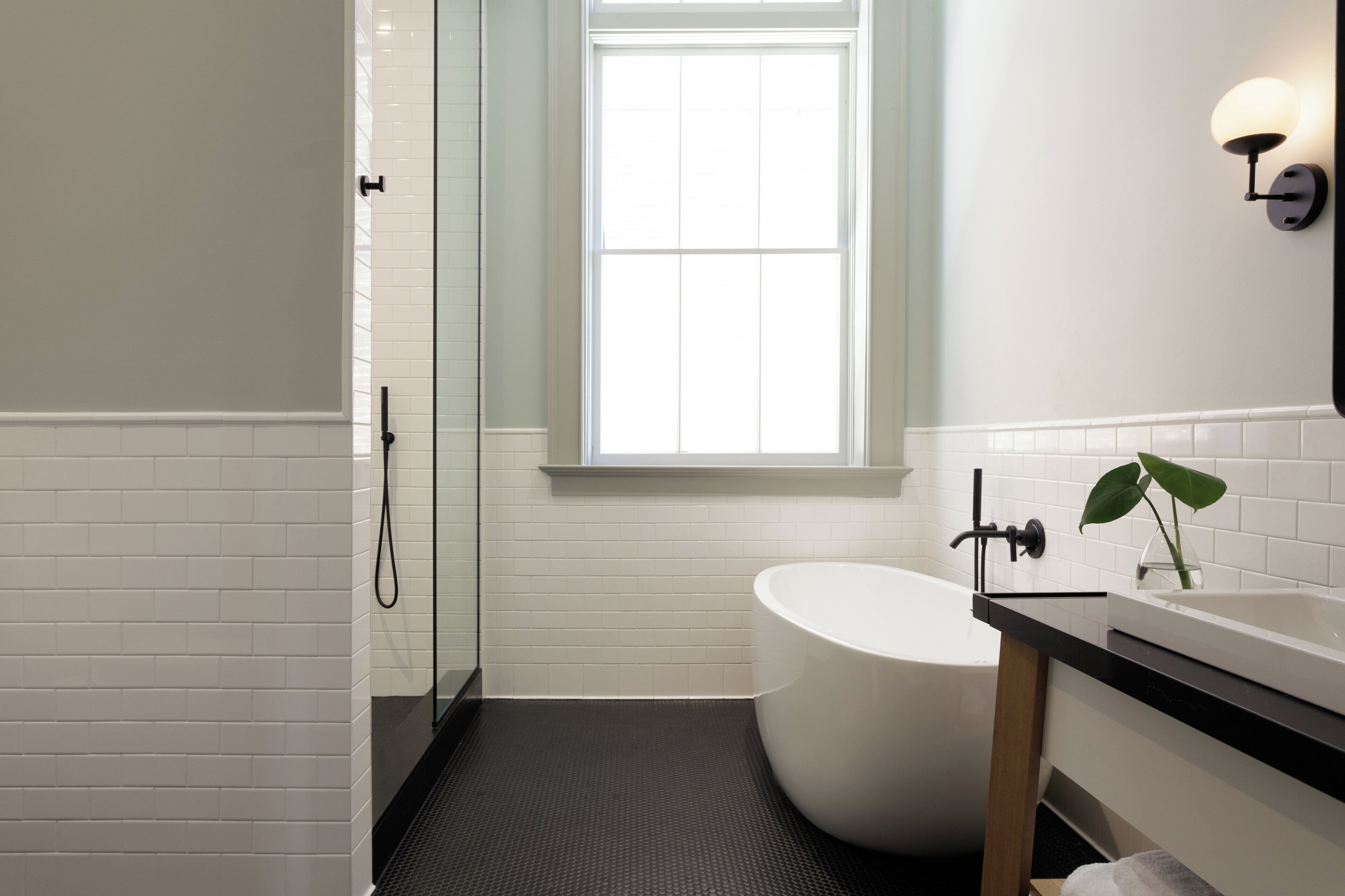 A modern bathroom with a freestanding bathtub, a shower, and a window providing natural light.