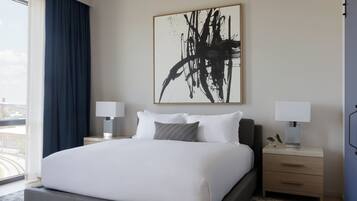 Habitación de hotel con una cama grande, dos mesitas de noche con lámparas, un cuadro abstracto de gran tamaño en la pared y vistas por la ventana.
