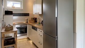 Eine moderne Küche mit einem Edelstahlkühlschrank, einem eingebauten Ofen und einer Spüle. Ein Holztisch mit einem Korb und einem Geschirrständer ist ebenfalls vorhanden.