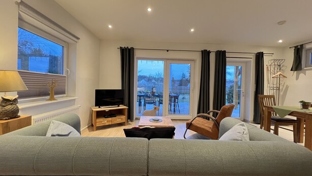 Ein Wohnzimmer mit Sofa, Fernseher und einem Esstisch mit Stühlen.