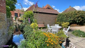 Un jardin agrémenté d’un bâtiment en briques, d’un étroit canal d’eau et de mobilier d’extérieur blanc.