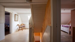 Un escalier menant à une chambre située en mezzanine, avec un plancher en bois et une rambarde blanche.