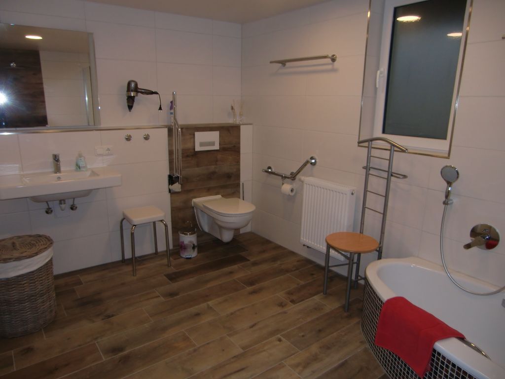 A bathroom with a wooden floor, white tiles, a sink, a toilet, a bathtub, and a mirror.
