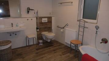 A bathroom with a wooden floor, white tiles, a sink, a toilet, a bathtub, and a mirror.