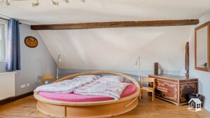 Une pièce comprenant un lit rond en bois, une commode en bois, un miroir et un radiateur.