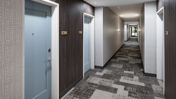 Corredor de hotel com carpete estampado, painéis de madeira escura e portas azuis claras.