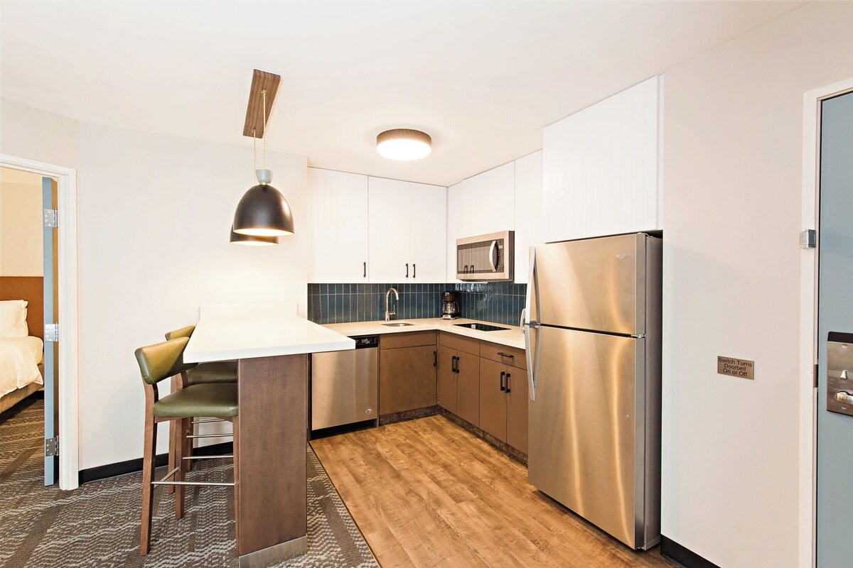 A compact kitchen with a microwave, refrigerator, and bar stools.