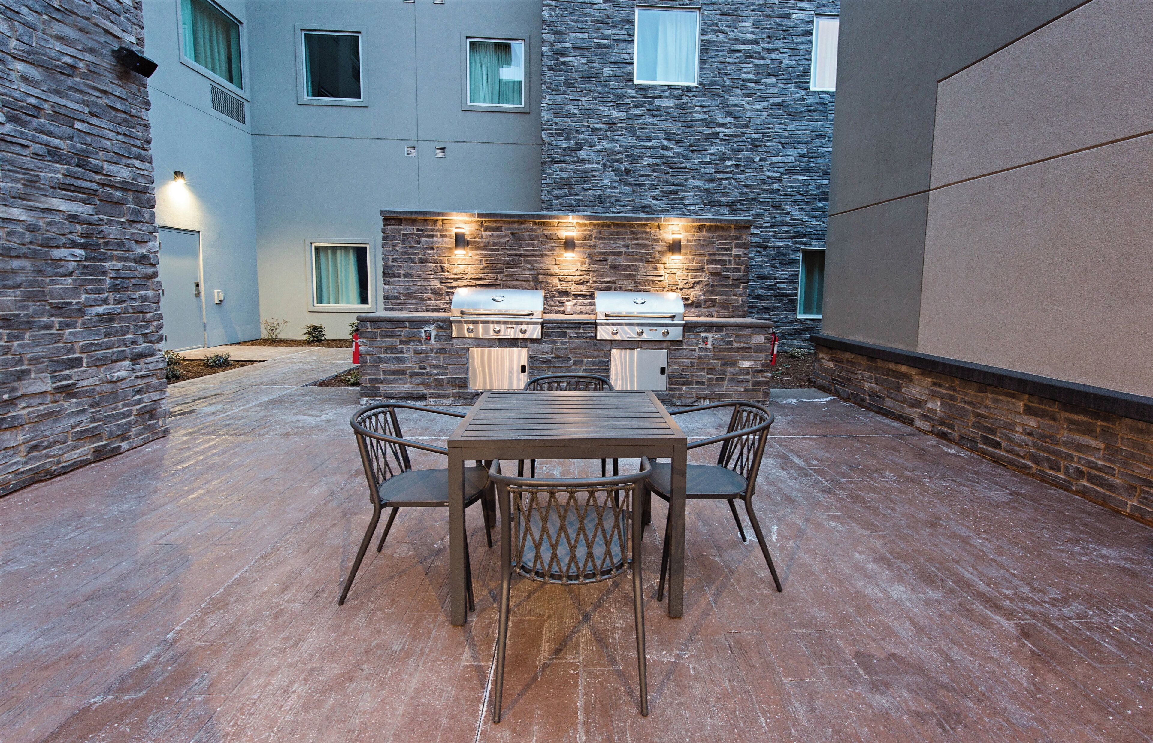Eine Terrasse im Freien mit einer Steinmauer, einem Grill und einem Tisch mit Stühlen.