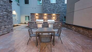 Un patio exterior con muro de piedra, una parrilla y una mesa con sillas.