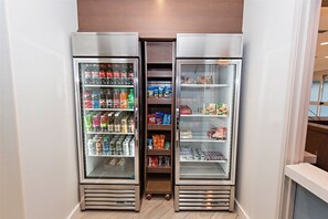 A row of three refrigerated display cases in a commercial setting, containing a variety of beverages and snacks. - Staybridge Suites Denver North - Thornton by IHG (Thornton)