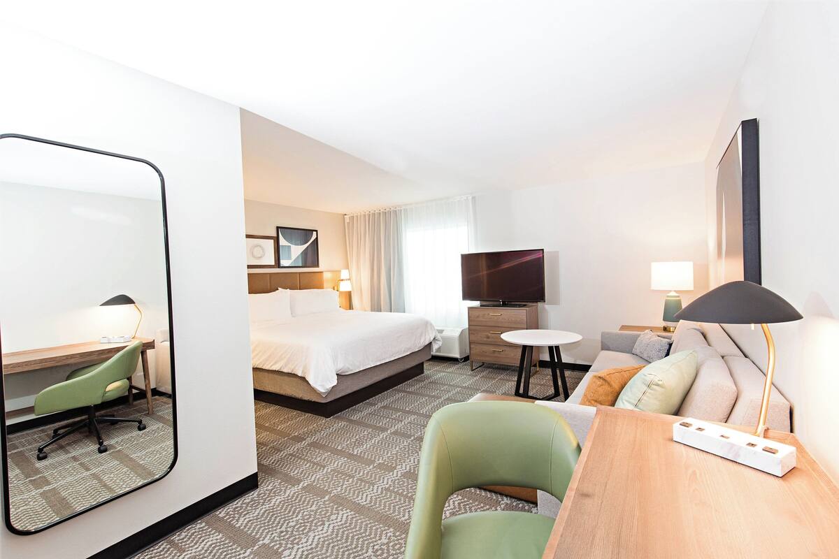 A hotel room with a bed, a desk, a chair, a TV, and a lamp.
