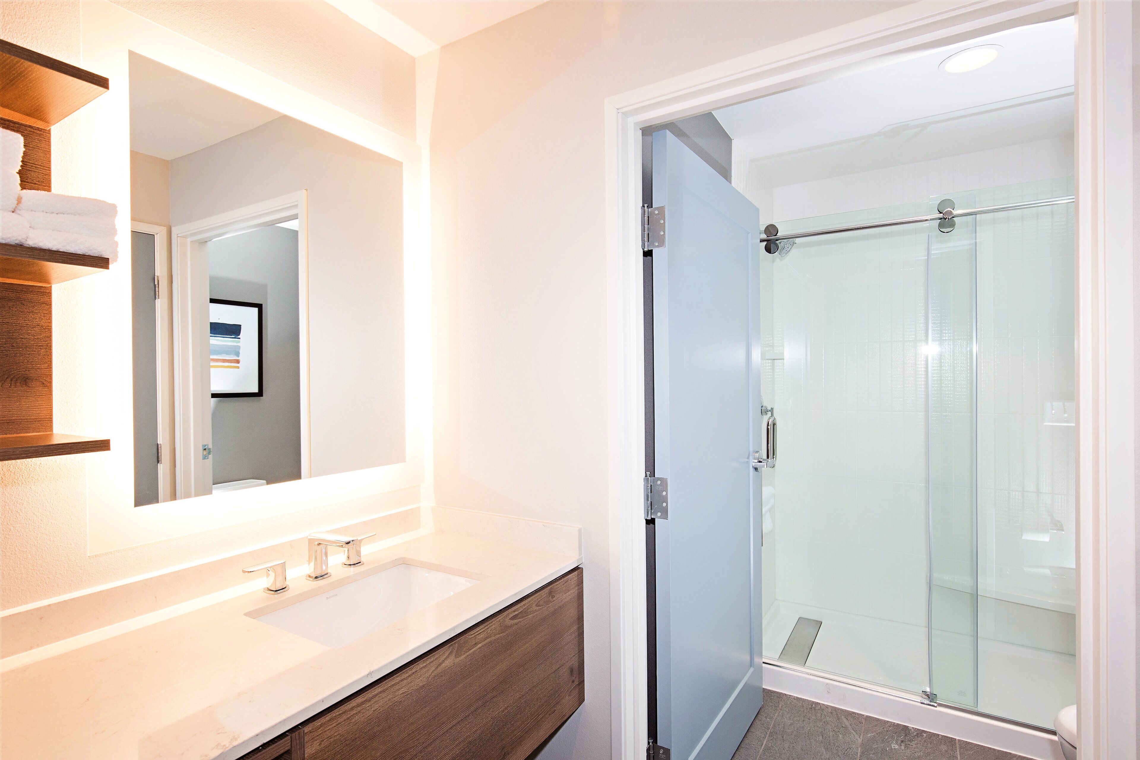 A bathroom with a white sink, wooden vanity, and a glass shower enclosure.